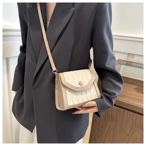 Détail d'un sac bandoulière beige matelassé porté avec un blazer gris élégant