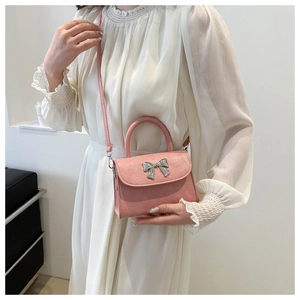 Detail of light pink crossbody bag with silver bow accent and leather strap on a model