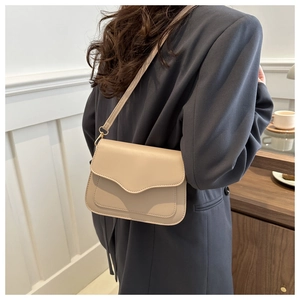 Detail view of cream minimalist crossbody bag with wavy flap design on a model
