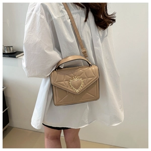 Close-up of beige quilted crossbody bag with golden crown heart clasp on a model