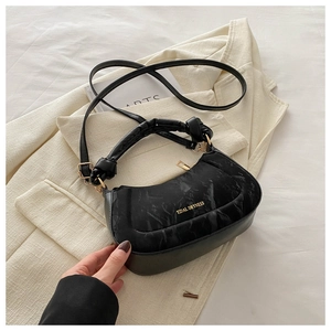 Detail of black leather handbag featuring gold Tidal Dryness lettering and pleated handle