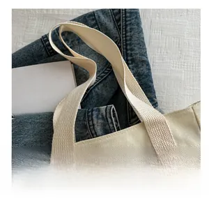 Detail of reinforced webbing handle and metal zipper on the beige canvas tote bag