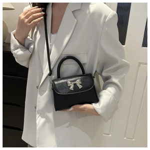 Detail of black bow handbag with silver charm and smooth faux leather texture
