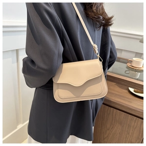 Side view of a beige matte leather crossbody bag with wave edge on a model in gray blazer
