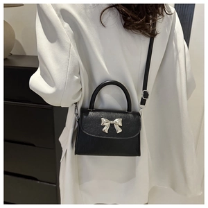 Detailed view of black pebbled leather texture and silver bow buckle on the small bag