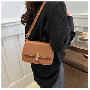 Brown faux leather crossbody bag with gold buckle shown on shoulder for sizing