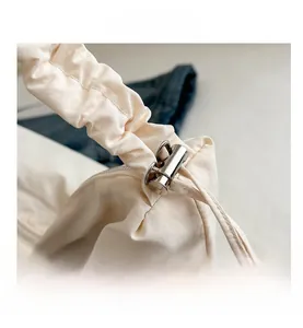 Detail of off-white canvas tote bag featuring adjustable scrunchie shoulder strap and buckle