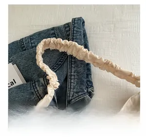 Detail shot of the ruched shoulder strap on a cream tote bag with denim background
