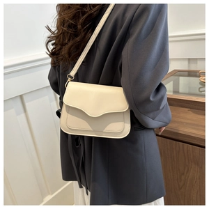 Detail of a creamy white leather crossbody bag with wavy flap edge on a model's shoulder