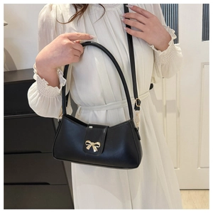 Close-up of black leather crescent bag featuring a delicate gold bow metal buckle