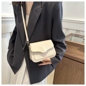 Detail of minimalist cream crossbody bag featuring a unique scalloped edge flap design