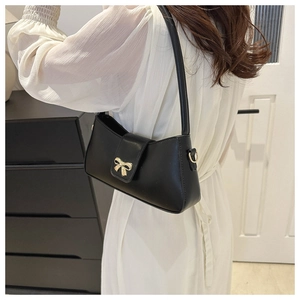 Détail d'un sac baguette noir avec boucle nœud doré porté par un mannequin