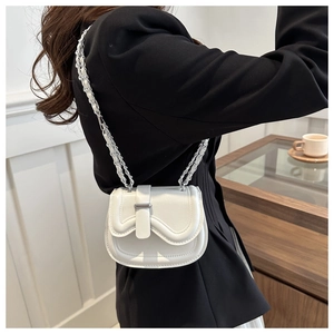 Close-up of a white leather saddle bag with wave edge flap and silver chain strap