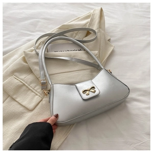 Detail of silver metallic underarm bag with elegant gold bow hardware on blazer