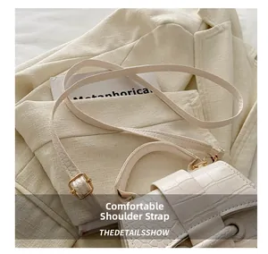 Detail of elegant crocodile-embossed leather strap and gold-tone metal buckle on white bag