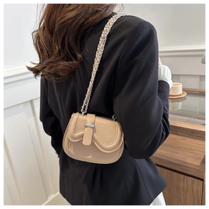 Close-up of mini saddle bag with wavy flap and silver chain on model in minimalist interior