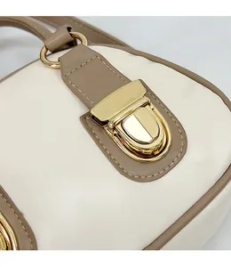 Detailed close-up of cream leather bag with brown trim and elegant gold metal buckle closure