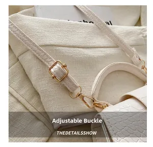 Detail of adjustable gold buckle and white crocodile embossed texture on a crossbody bag