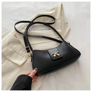 Detail view of a black leather baguette bag featuring a gold metal bow buckle on fabric