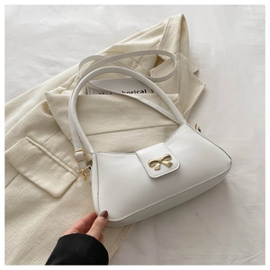 Detail of white leather baguette bag featuring a gold bow-shaped metal buckle and strap