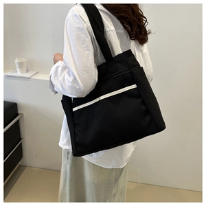 Detail of a large black canvas tote bag featuring white contrast stripes and side pockets
