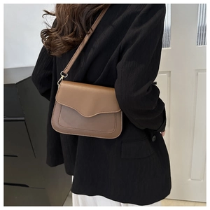 Detail of a brown minimalist crossbody bag with a wavy flap design worn by a model