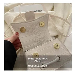 Close-up of the golden magnetic buckle and crocodile embossed texture on a white bag
