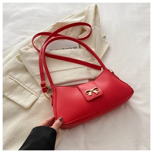 Close-up of red leather shoulder bag with decorative golden bow metal buckle details