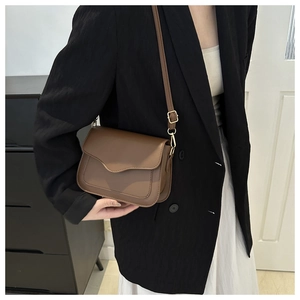 Brown leather crossbody bag detail featuring wave-edge flap and golden buckle on model