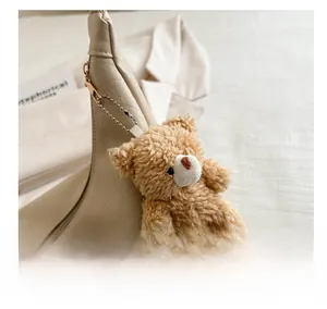 Close-up of a brown fuzzy teddy bear charm attached to a beige leather shoulder bag zipper