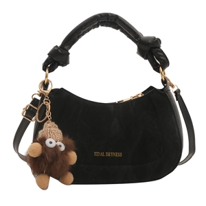 Black crescent handbag with knotted handle and brown plush monster charm on white background