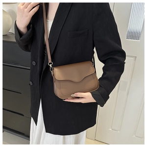Detail of a brown crossbody bag with unique wave-shaped flap and matte finish