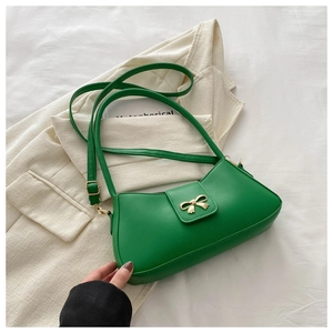 Detail of a bright green patent leather baguette bag with a gold metal bow ornament