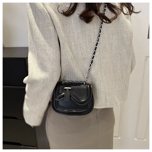 Detail of black mini crossbody bag featuring wavy flap design and silver metal buckle