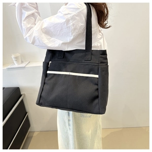 Dettaglio borsa tote in tela nera con tasche laterali e striscia bianca a contrasto