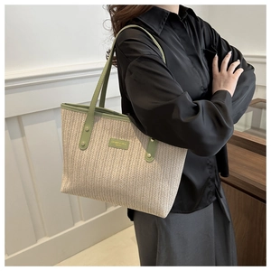 Close-up of woven straw tote bag with green leather trim and golden metal rivet details