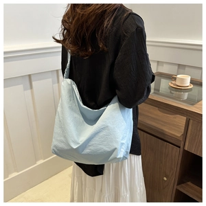 Detail of light blue pleated canvas tote bag worn by model in a minimal indoor setting