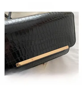 Detailed close-up of glossy black crocodile pattern leather bag with gold metal bar