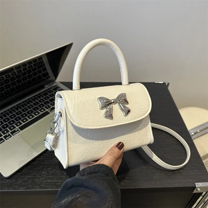 Chic cream bow handbag with silver metal knot and detachable strap on office desk