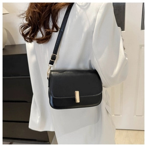 Detail view of black leather crossbody bag with polished gold buckle on white blazer