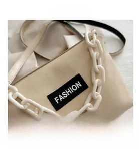 Detail of cream crossbody bag featuring a thick white chain and fashion patch