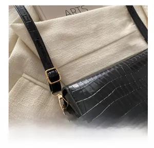 Detail shot of golden metal hooks and adjustable buckle on black croc-effect crossbody bag
