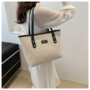Large woven tote bag with black leather trim and handles on model in minimalist interior