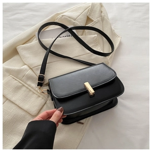 Detail of a matte black leather crossbody bag with a gold rectangular metal buckle