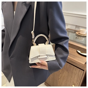 Close-up of white croc-embossed trapezoid bag with reinforced top handle on a model
