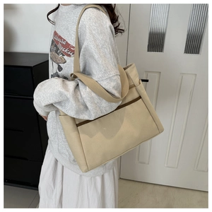 Detail of a large beige canvas tote bag with brown trim pockets and wide shoulder straps