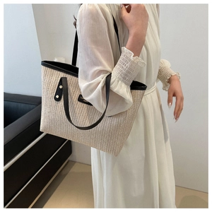 Detail of straw tote bag with black leather handles and herringbone weave texture