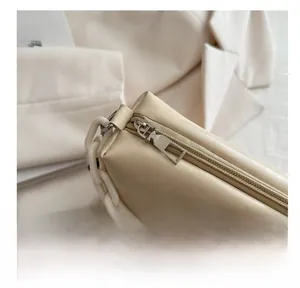 Detail of smooth metal zipper and white plastic chain on a beige leather crossbody bag