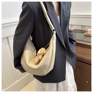 Detail of a beige crescent hobo bag with PU leather texture and a small plush bear charm