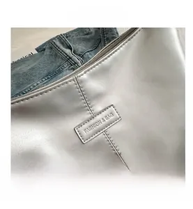 Detail view of silver metallic textured fabric and embossed fashion label on shoulder bag